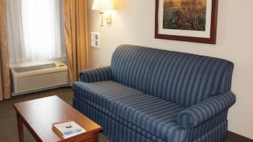 Una camera d'albergo con un divano a righe blu, un tavolino con un libro, una finestra con tende, una lampada a parete e un quadro incorniciato.