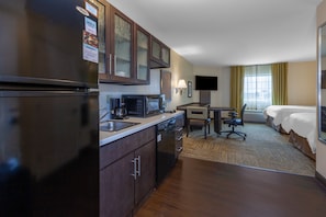 Une chambre d’hôtel équipée d’une kitchenette, d’un lit, d’un bureau et d’une télévision.