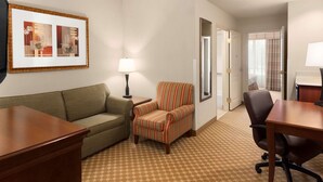 Ein Hotelzimmer mit einem grünen Sofa, einem gestreiften Sessel, einem Holztisch und einem Spiegel an der Wand.