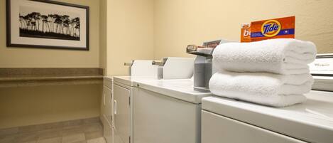 A hotel laundry area with a stacked white towel, a Tide detergent box, and a framed picture on the wall.