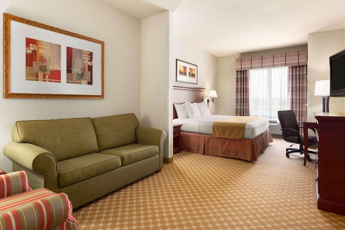 A hotel room with a green sofa, a bed with a red and white striped bedspread, a desk with a computer, and a television.