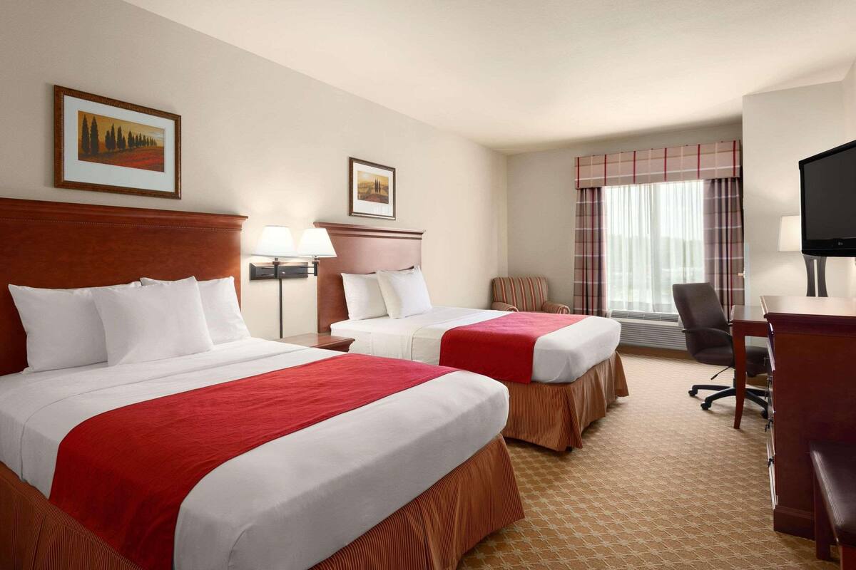 A hotel room with two beds, a desk, a chair, and a television.
