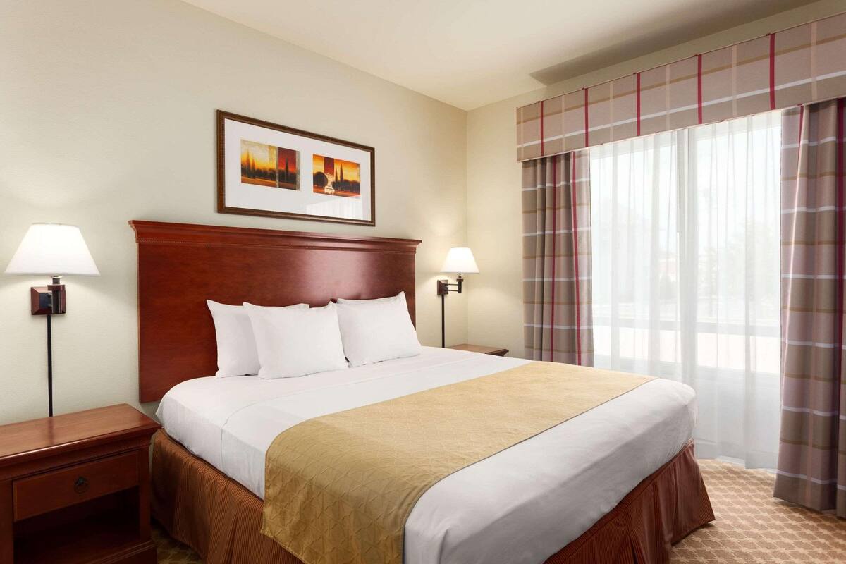 A hotel room with a large bed, two bedside tables, a headboard, and a framed picture above the bed.