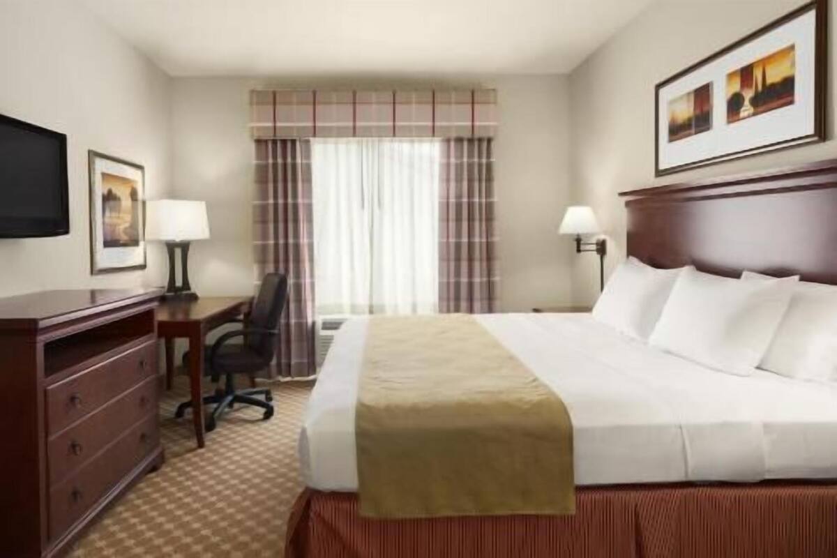 A hotel room with a bed, a desk, a chair, a TV, and a window with curtains.