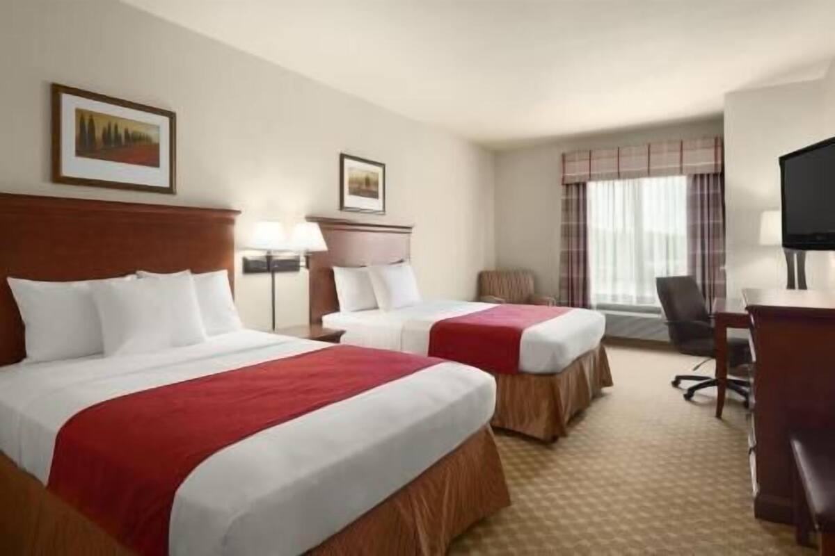 A hotel room with two beds, a desk, a chair, a television, and a window with curtains.