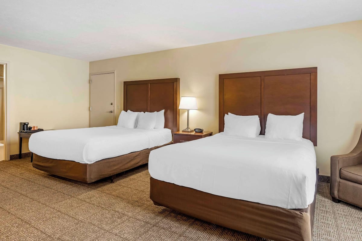 A hotel room with two beds, a nightstand with a lamp, and a chair.
