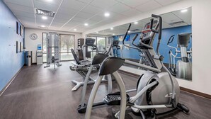 Een fitnessruimte met cardioapparaten, een waterdispenser en een klok aan de muur.