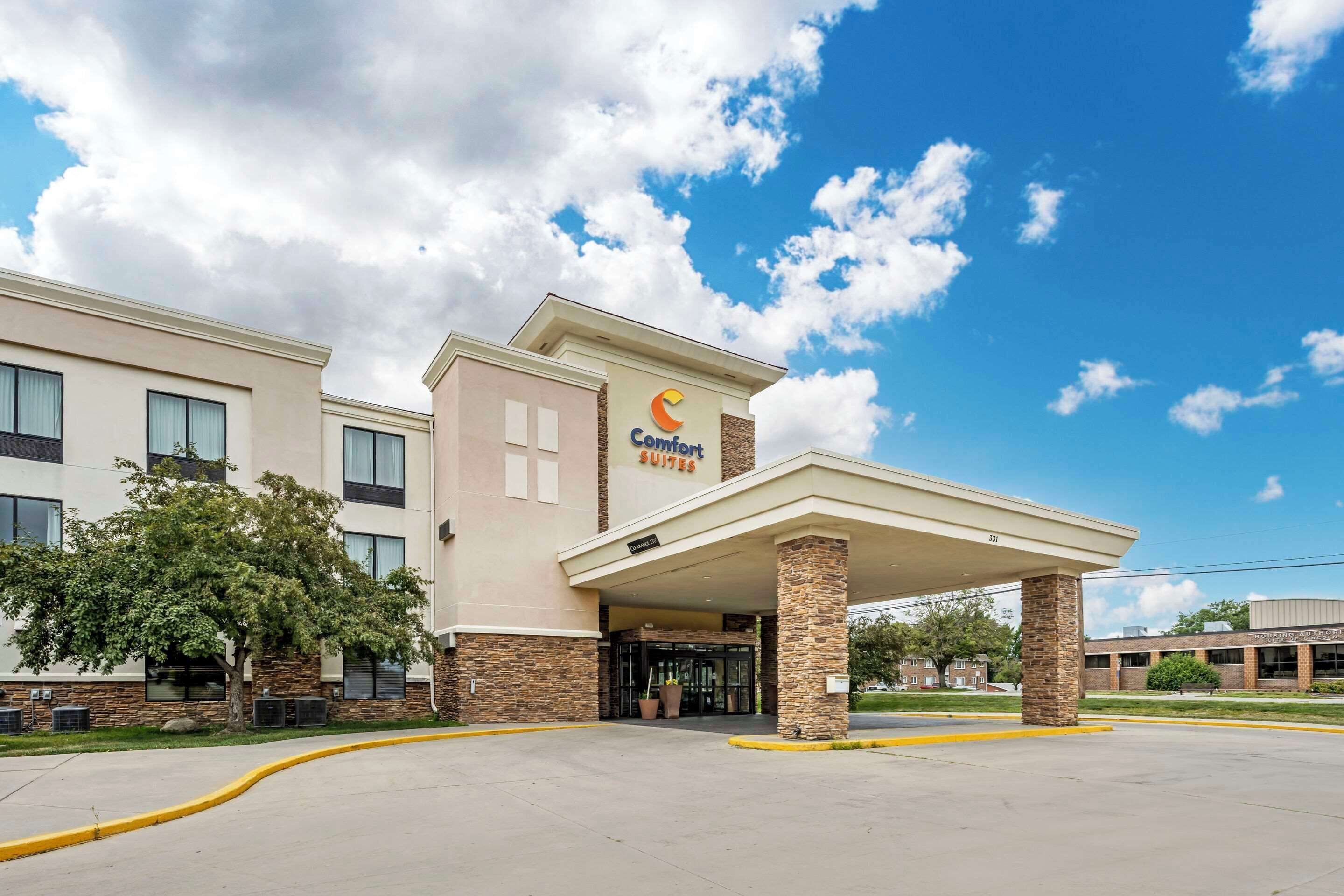 A Comfort Suites hotel with a covered entrance, stone pillars, and a clear blue sky.
