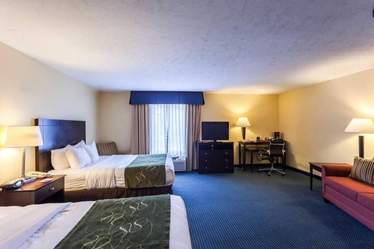 A hotel room with two beds, a desk, a chair, a sofa, and a television.