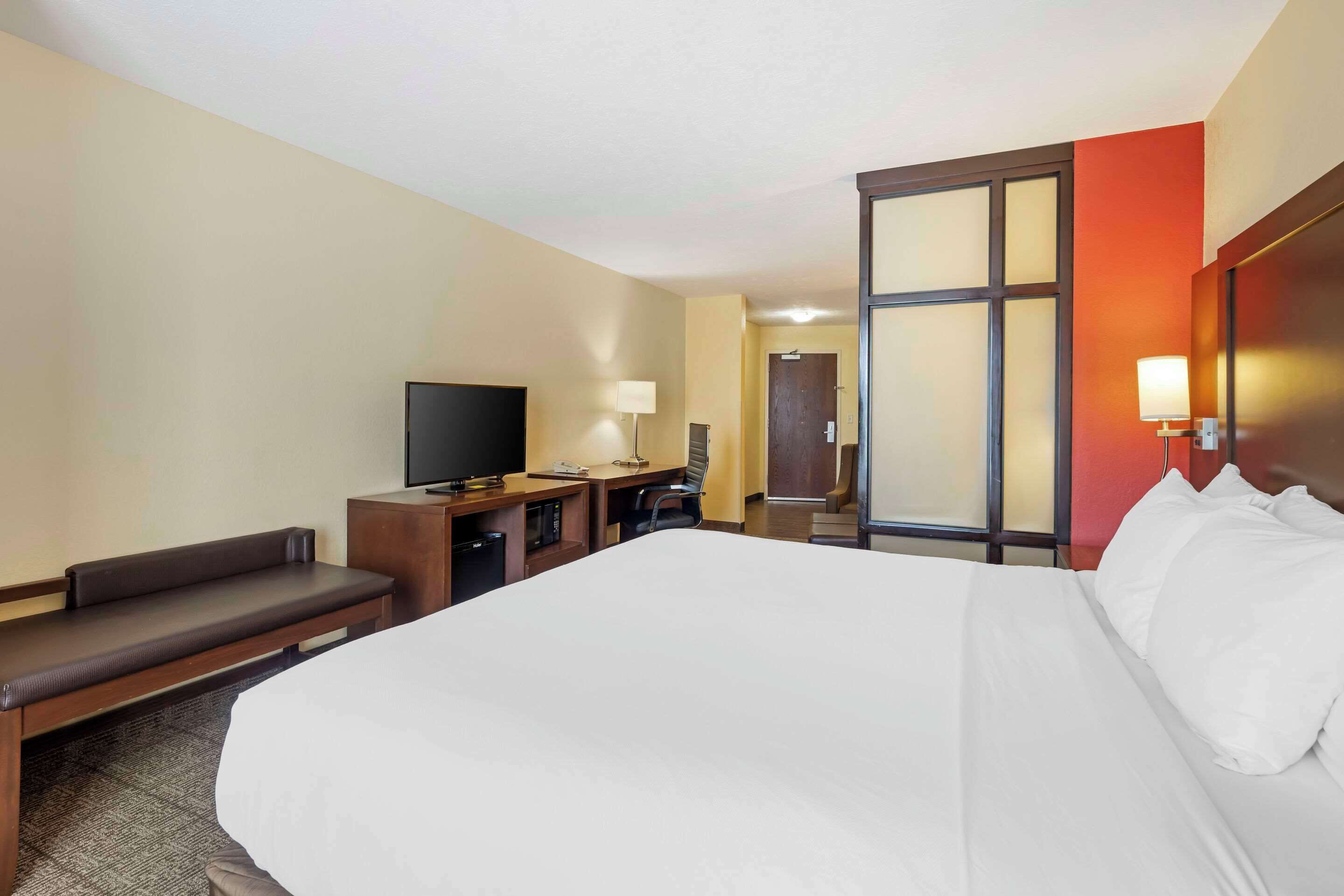 A hotel room with a large bed, a desk with a chair, a television, and a window with a view of the outside.