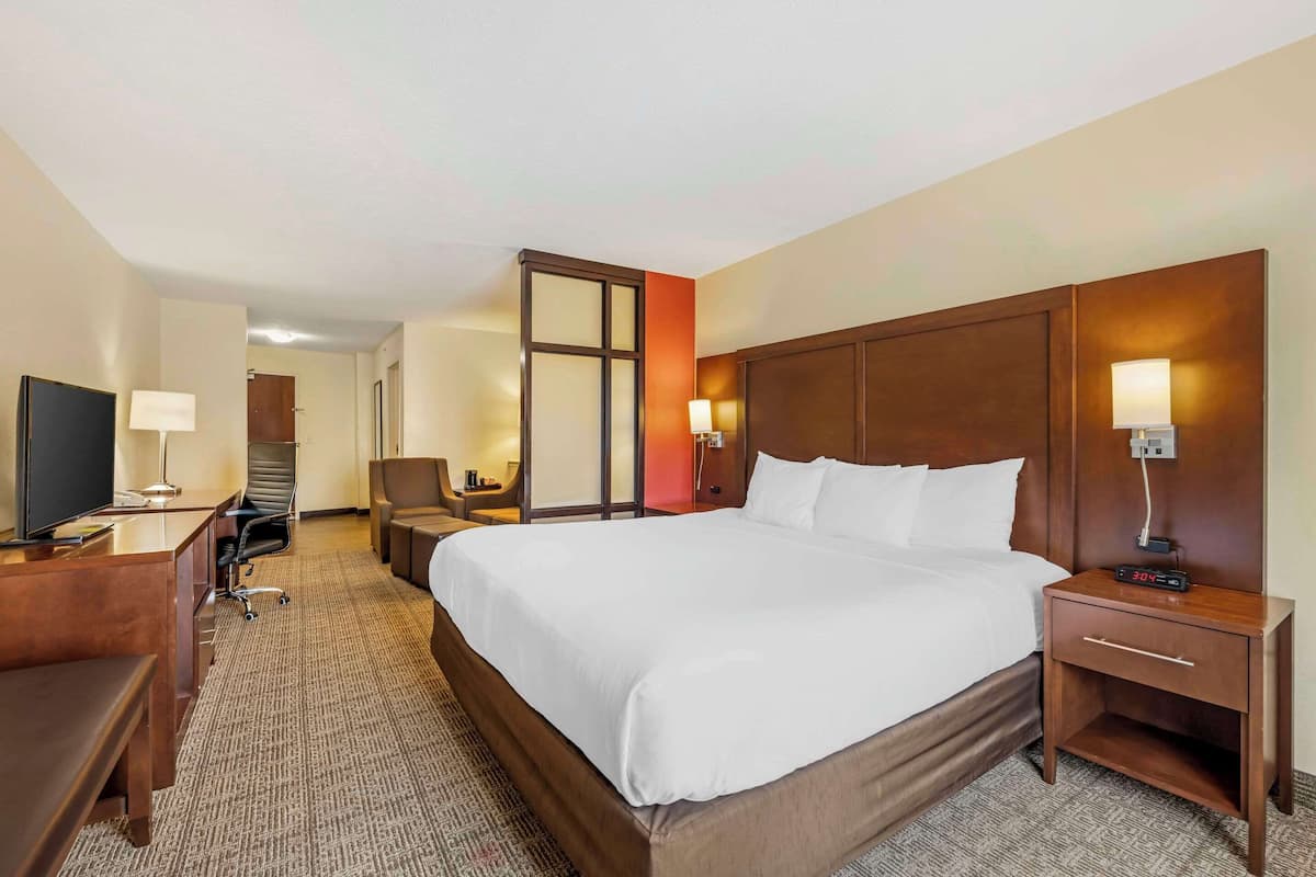 A hotel room with a large bed, a desk with a chair, a TV, and a desk lamp.