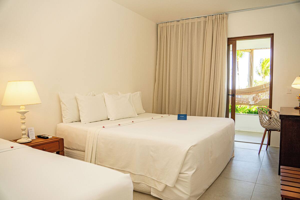 A hotel room with a bed, a nightstand, a lamp, a chair, and a view of the outdoors.