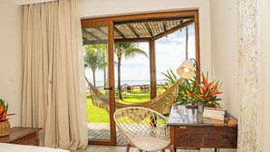 A room with a bed, a desk with a lamp, a chair, a view of a beach, and a hammock.