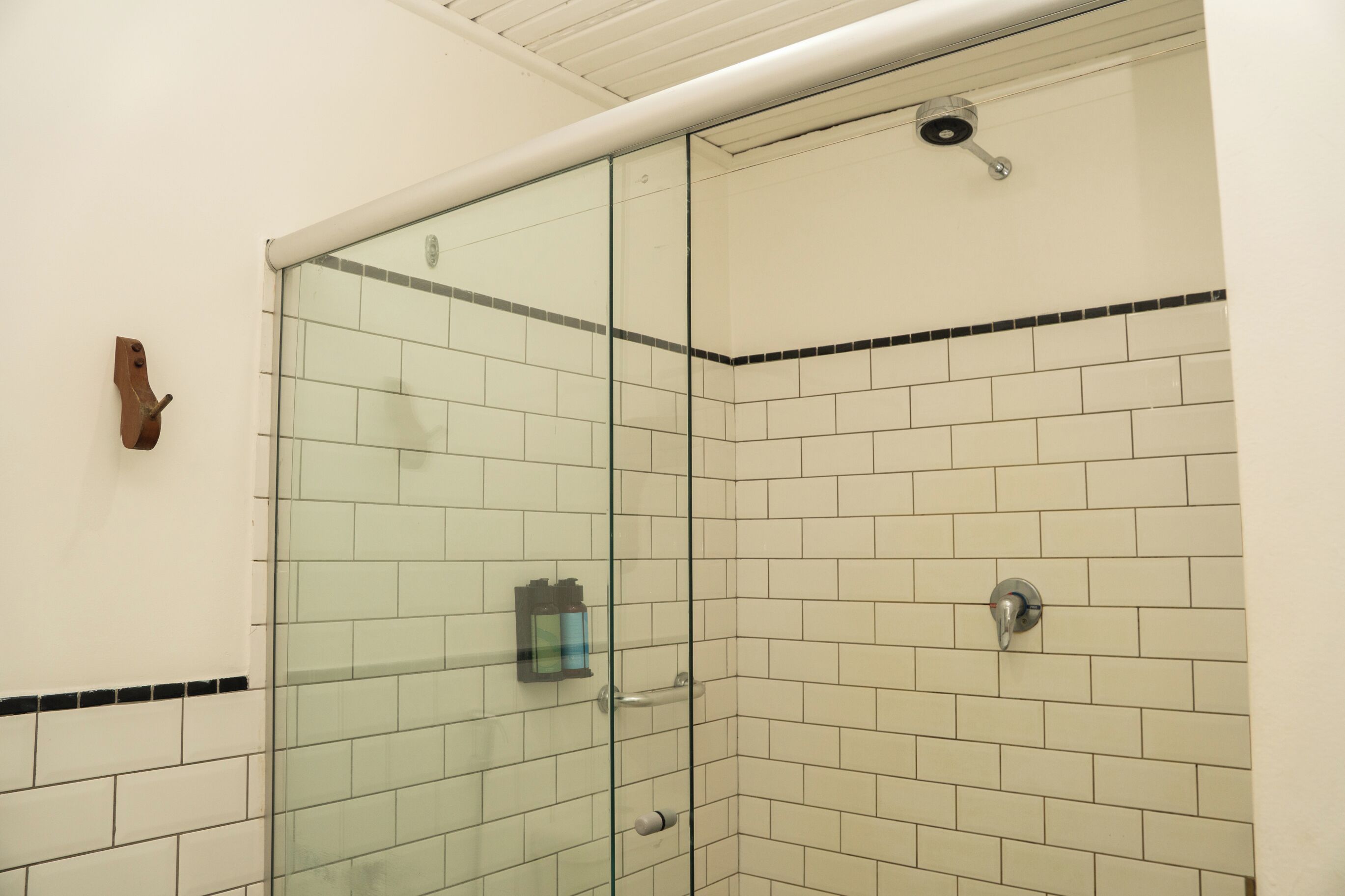 A glass-enclosed shower stall with white tiled walls and a black border, a towel rack, and a showerhead.
