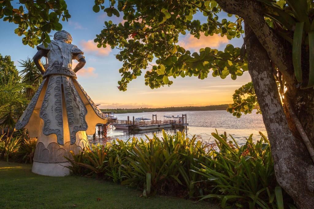 A statue of a woman in a dress by a lake with a dock and boats.
