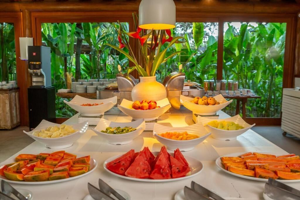 Une table de buffet garnie de divers fruits et légumes, une machine à café et un vase rempli de fleurs.