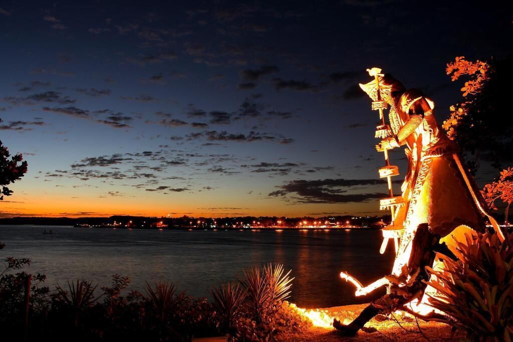 Vista nocturna de un muelle con una estatua iluminada con luces artificiales.