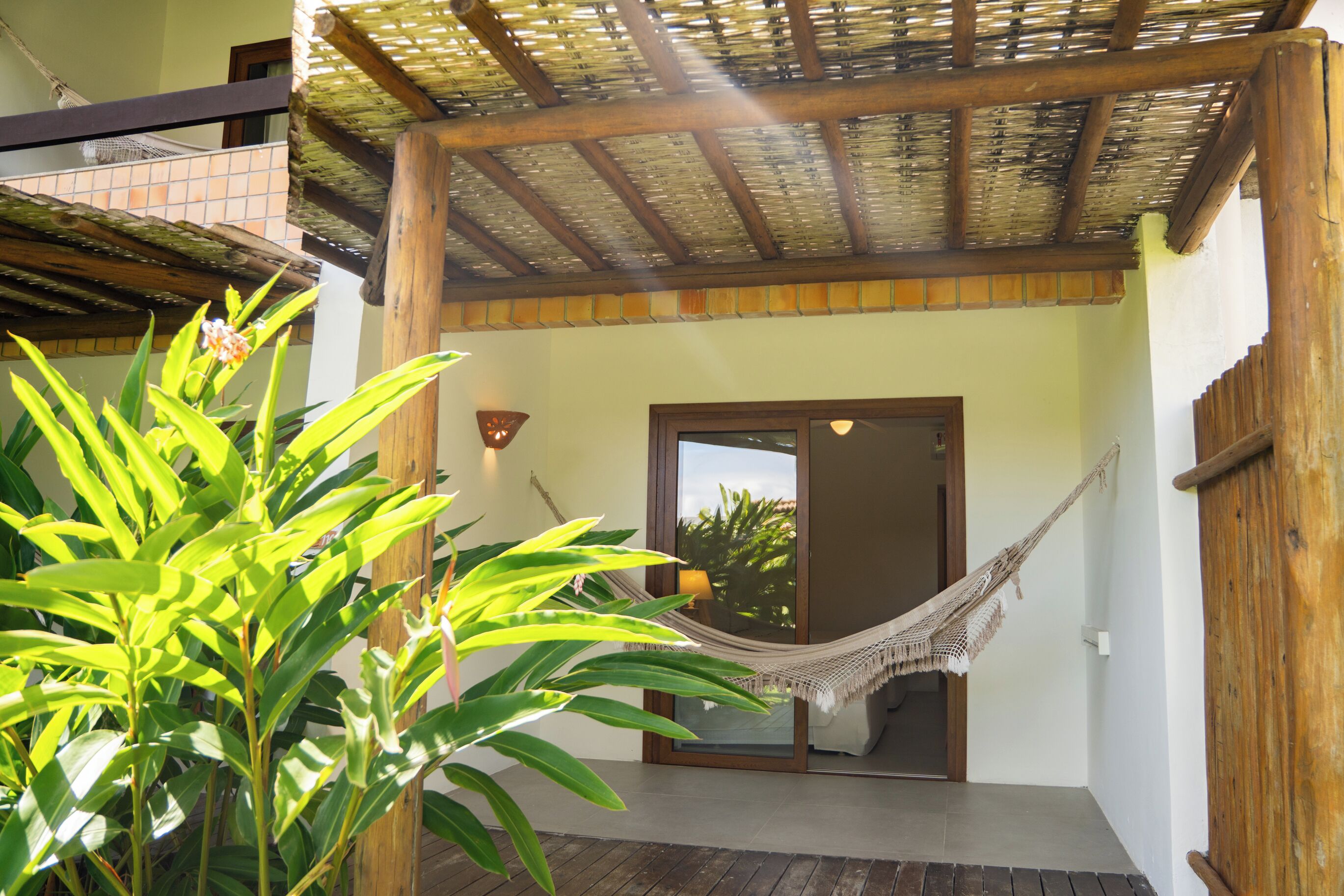 A wooden pergola with a hammock, a potted plant, and a view of the outside.