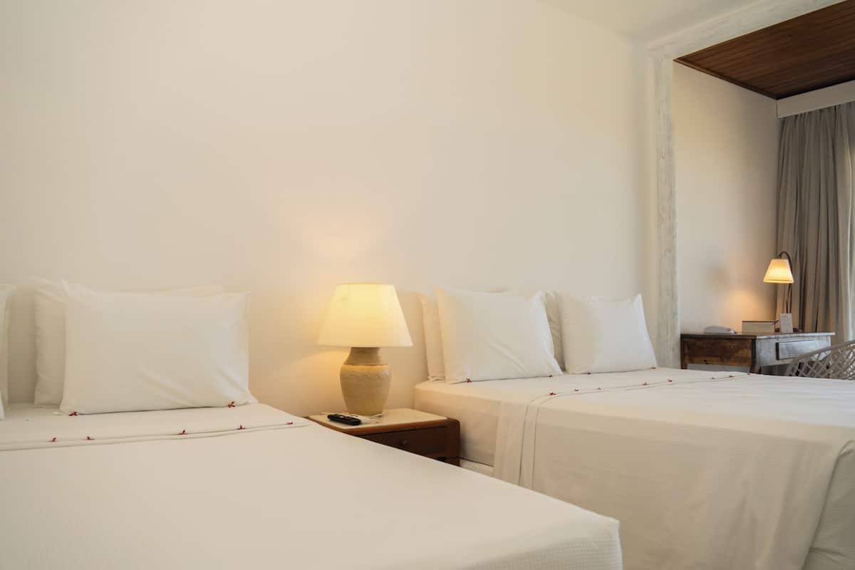 A hotel room with two beds, a nightstand with a lamp, a wooden headboard, and a window with curtains.