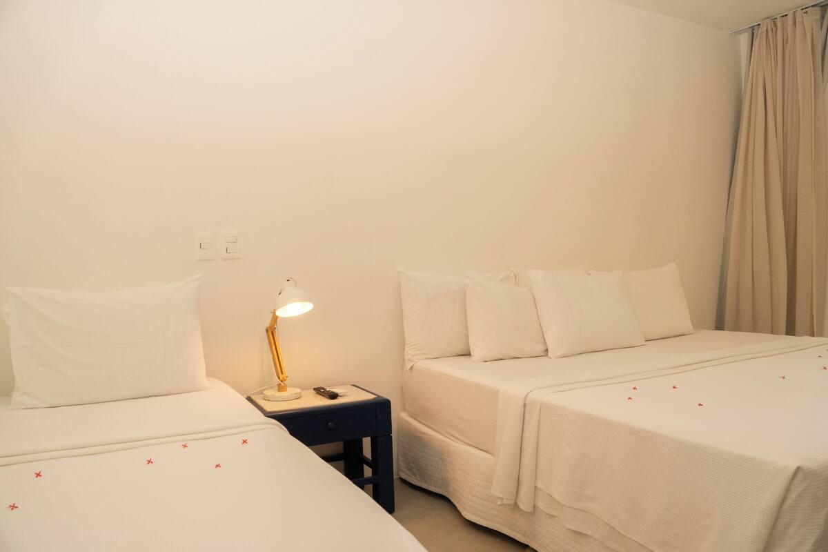 A hotel room with two beds, a nightstand with a lamp, and a curtain.