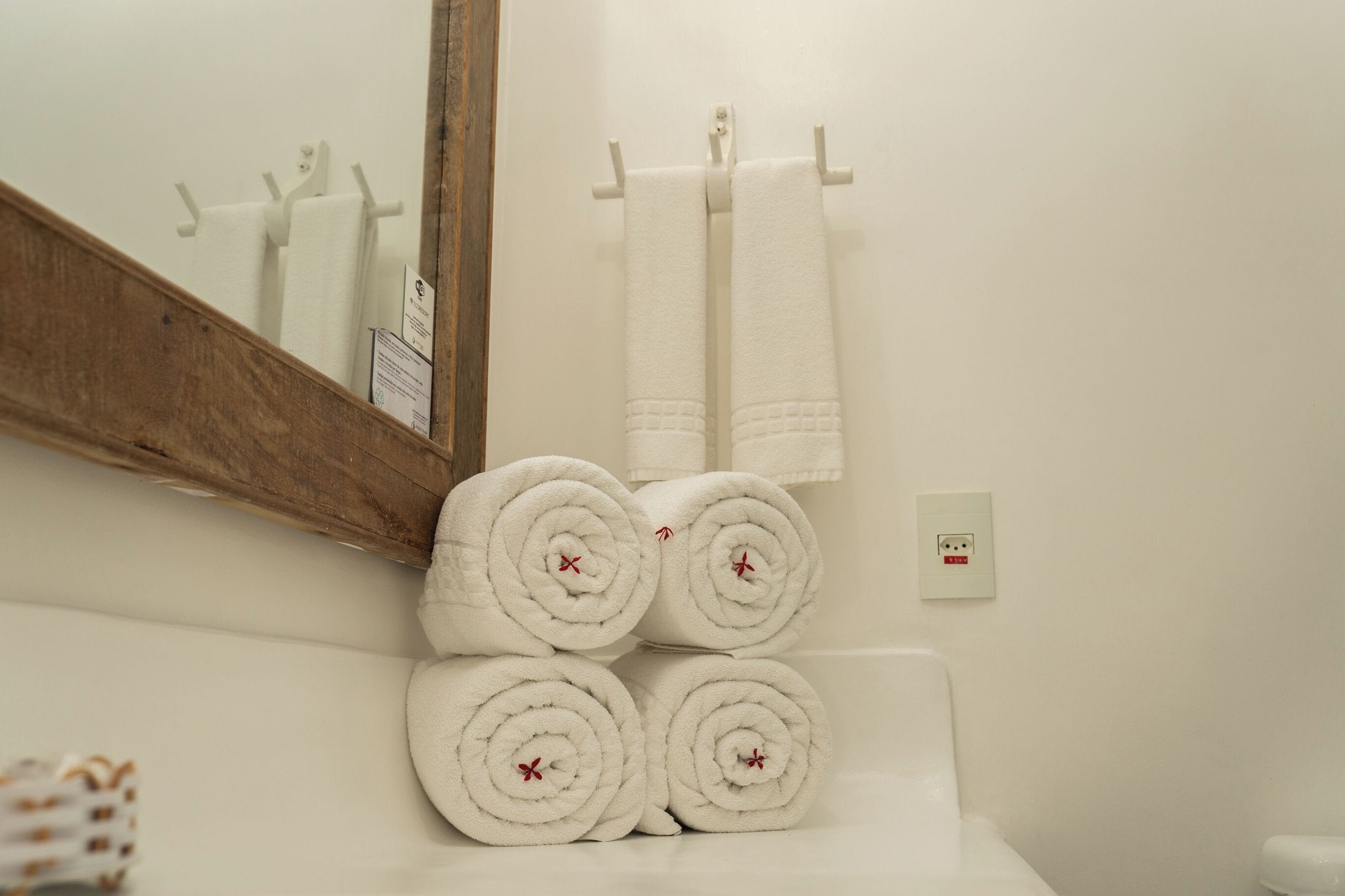 A bathroom with a wooden vanity, a mirror, and four neatly rolled white towels stacked on the vanity.