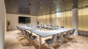 Un salón de conferencias con una larga mesa, sillas y una pantalla de televisión.