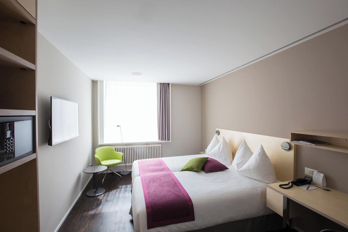 A hotel room with a bed, a desk, a chair, a television, and a window.