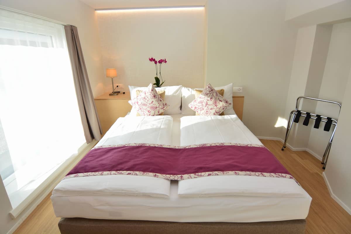 A neatly made double bed with a purple throw blanket, a bedside table with a lamp, and a wall-mounted radiator.