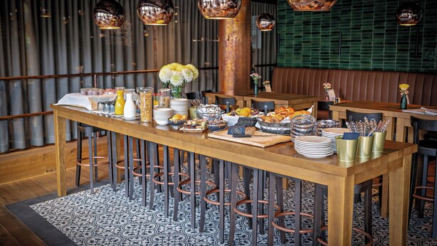 Un restaurante con una larga mesa de madera servida con varios platos, un suelo estampado y modernos taburetes de bar.