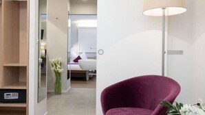 Una habitación de hotel moderna con un sillón morado, una mesita de noche y una lámpara.