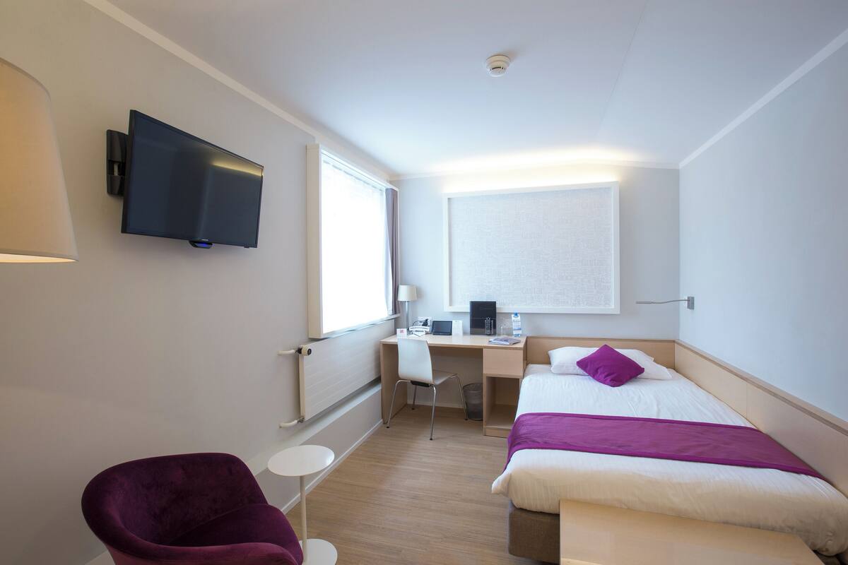 A hotel room with a bed, a desk, a chair, a TV, and a window.