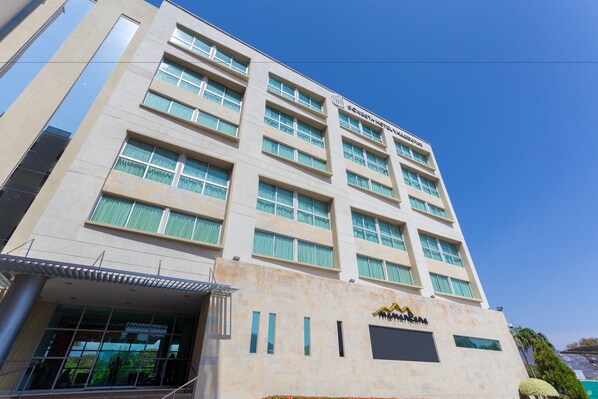Un hotel de varios pisos con un diseño arquitectónico moderno, que presenta una entrada destacada con una zona cubierta y ventanas amplias.