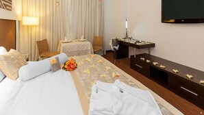 Habitación de hotel con cama, escritorio, televisión y ventana con cortinas.