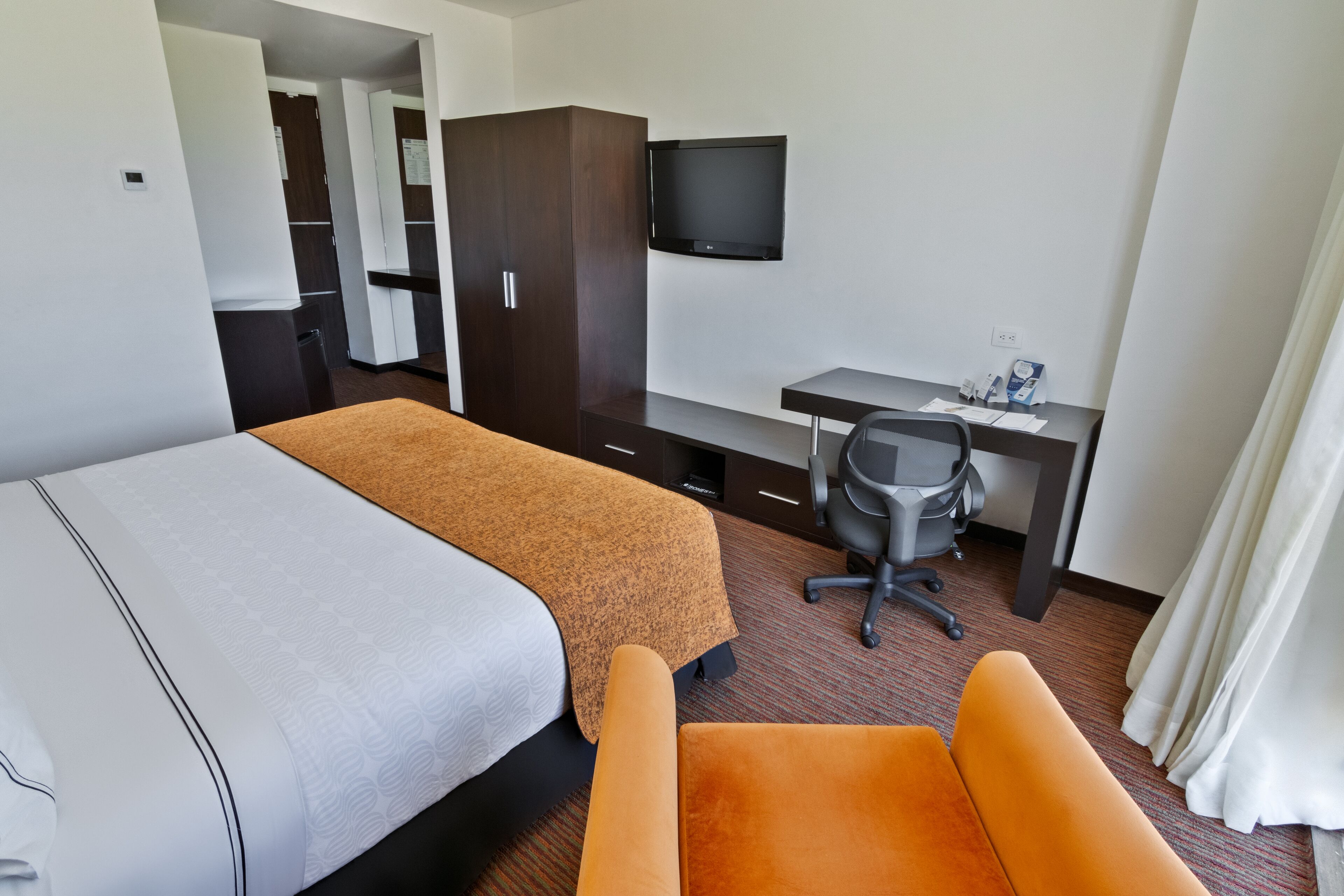 A hotel room with two beds, a desk, a chair, a television, and a wardrobe.
