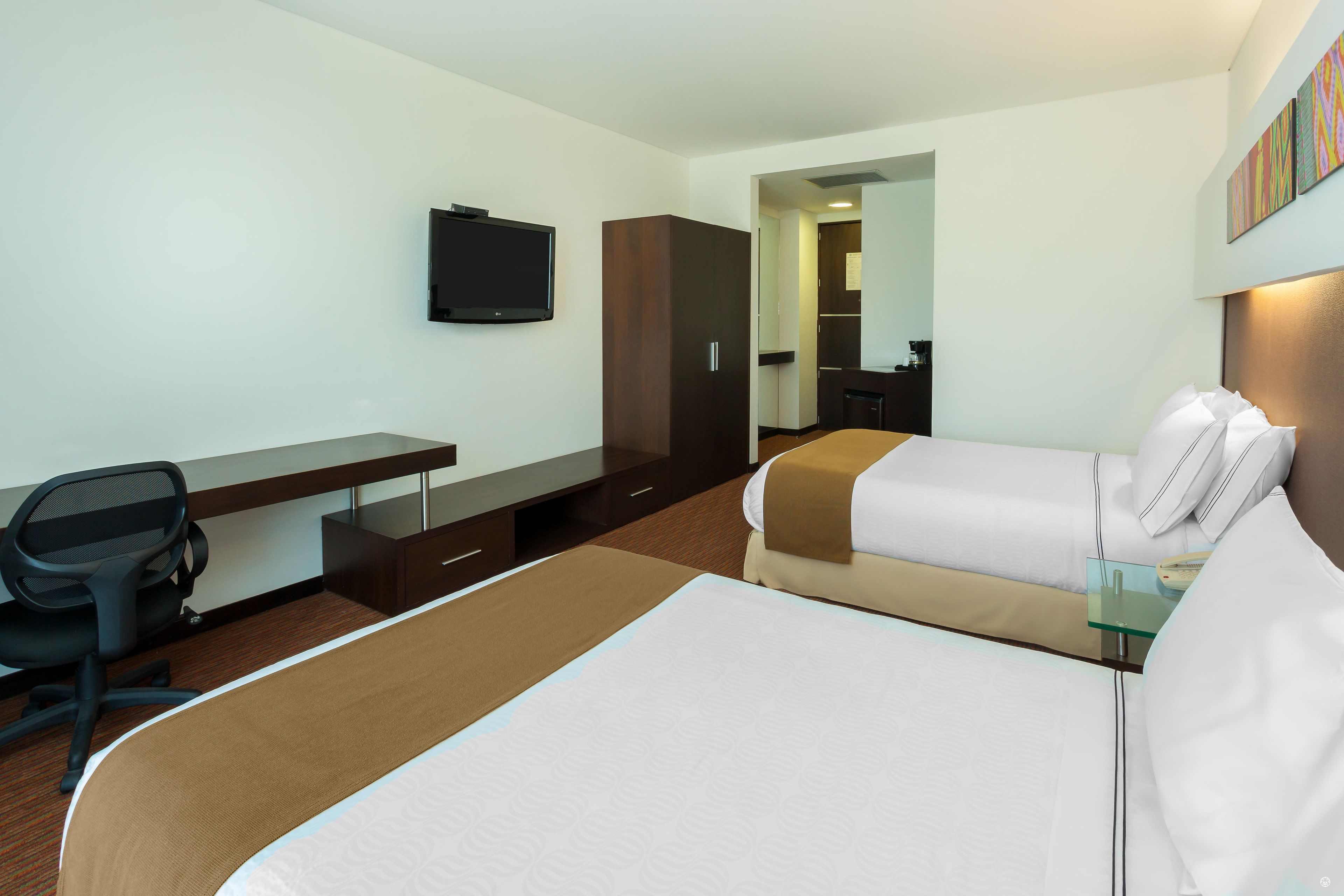 Habitación de hotel con una cama grande, un escritorio con una silla, un televisor y un armario.
