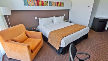 Una habitación de hotel con una cama, un sillón naranja, un escritorio con una lámpara y un televisor pequeño.