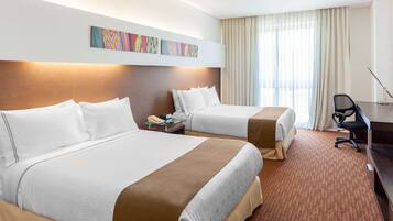 A hotel room with two beds, a desk, a chair, and a large window with curtains.