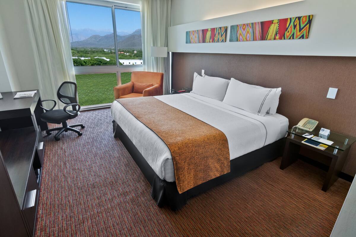 A hotel room with a large bed, a desk, a chair, and a view of the mountains.