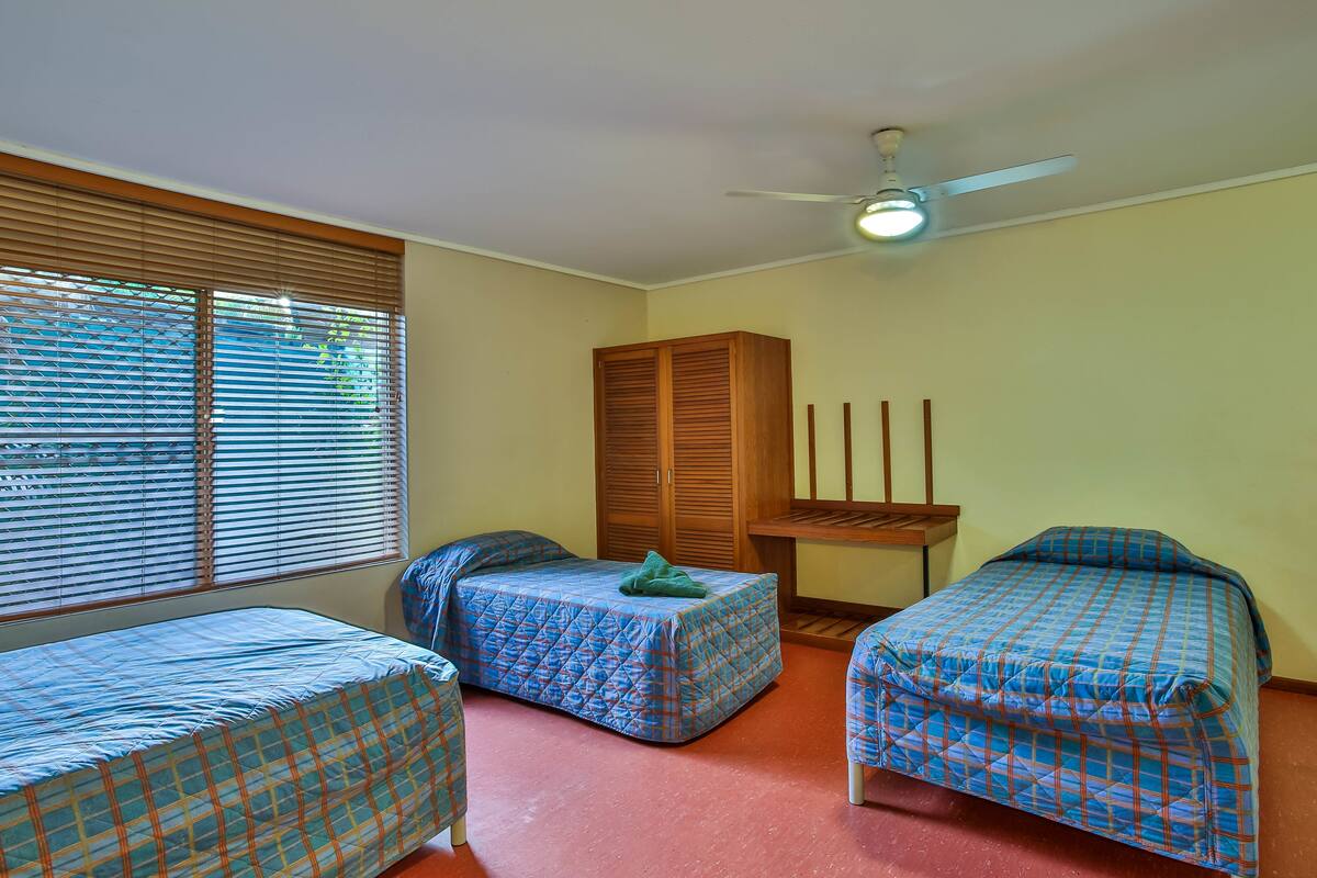 Une chambre avec deux lits simples, une armoire et un ventilateur de plafond.
