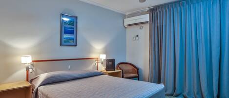 A hotel room with a bed, nightstands, a desk, a chair, a ceiling fan, and a window with curtains.