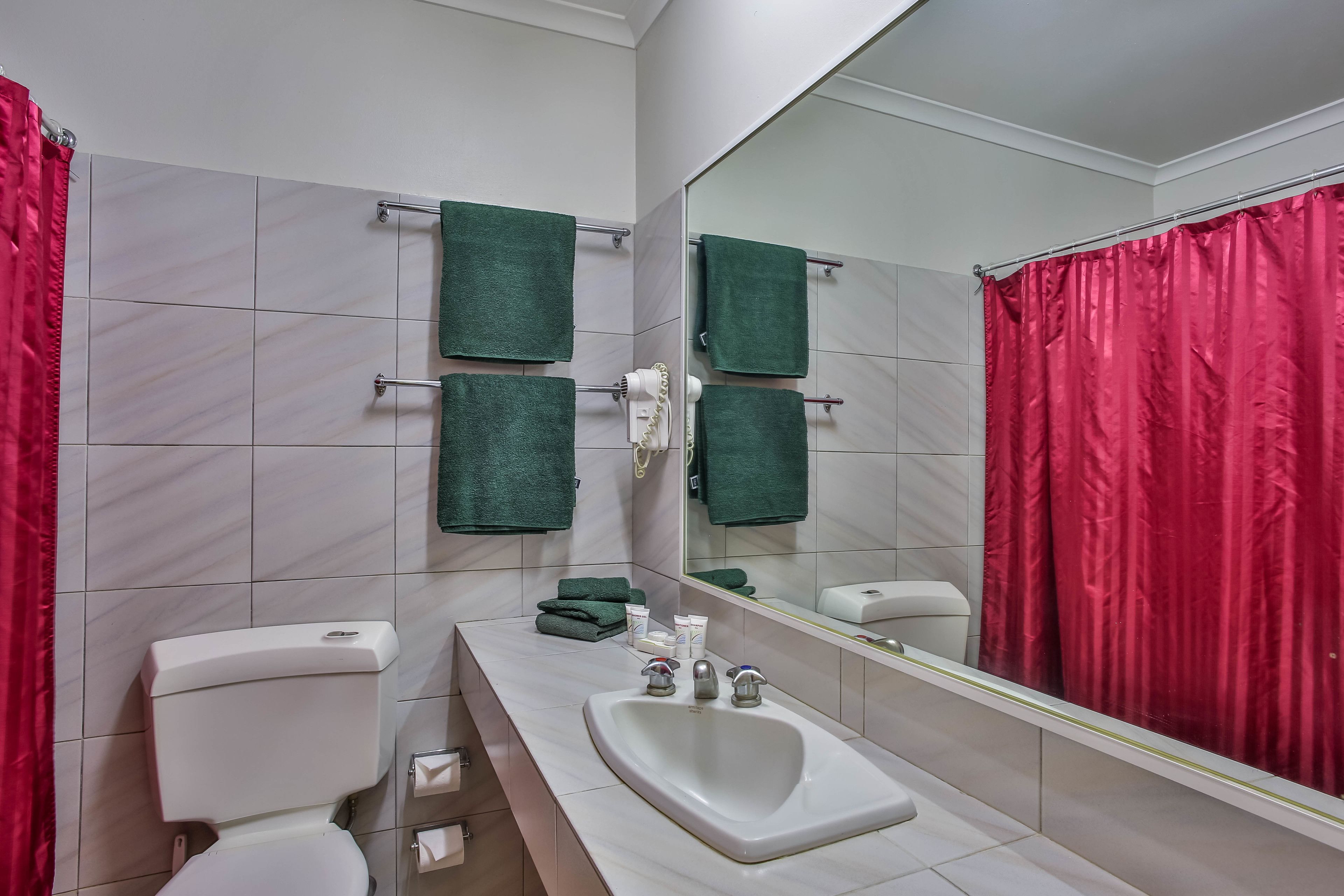A bathroom with a white sink, a toilet, and a mirror. There are green towels hanging on a rack, and a red shower curtain.