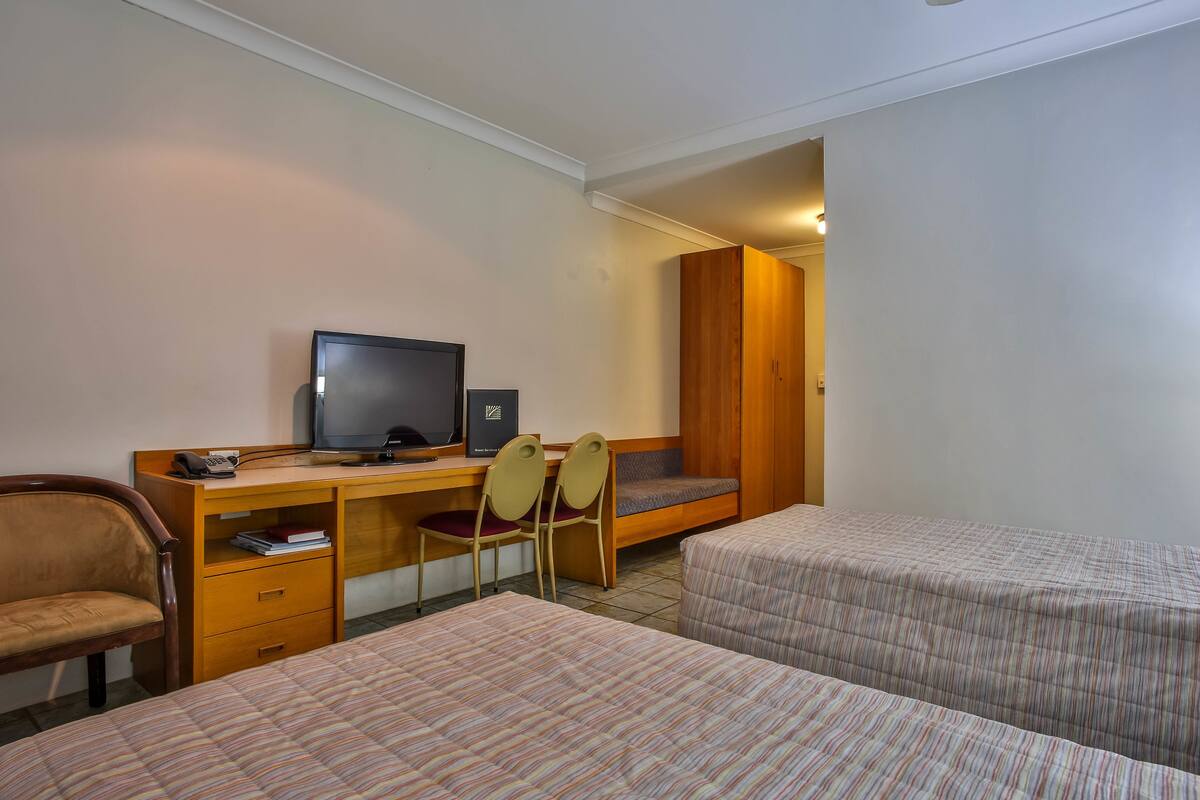 Une chambre d’hôtel avec deux lits, un bureau équipé d’un ordinateur et d’une chaise, et un téléviseur.