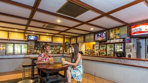 Zona de bar con taburetes, una barra y televisores mostrando deportes.