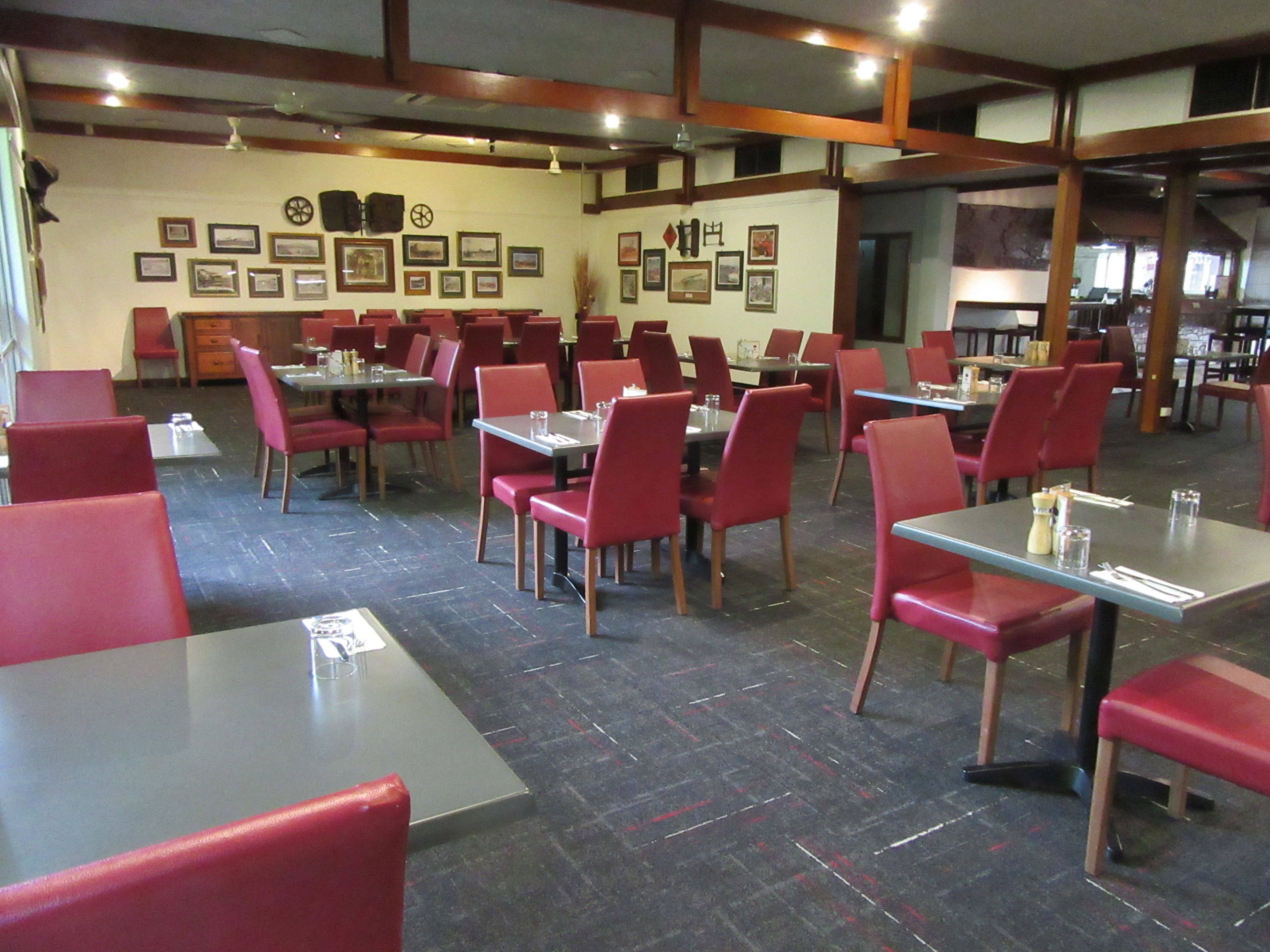 Un restaurante con sillas y mesas rojas, vigas de madera en el techo y cuadros en las paredes.