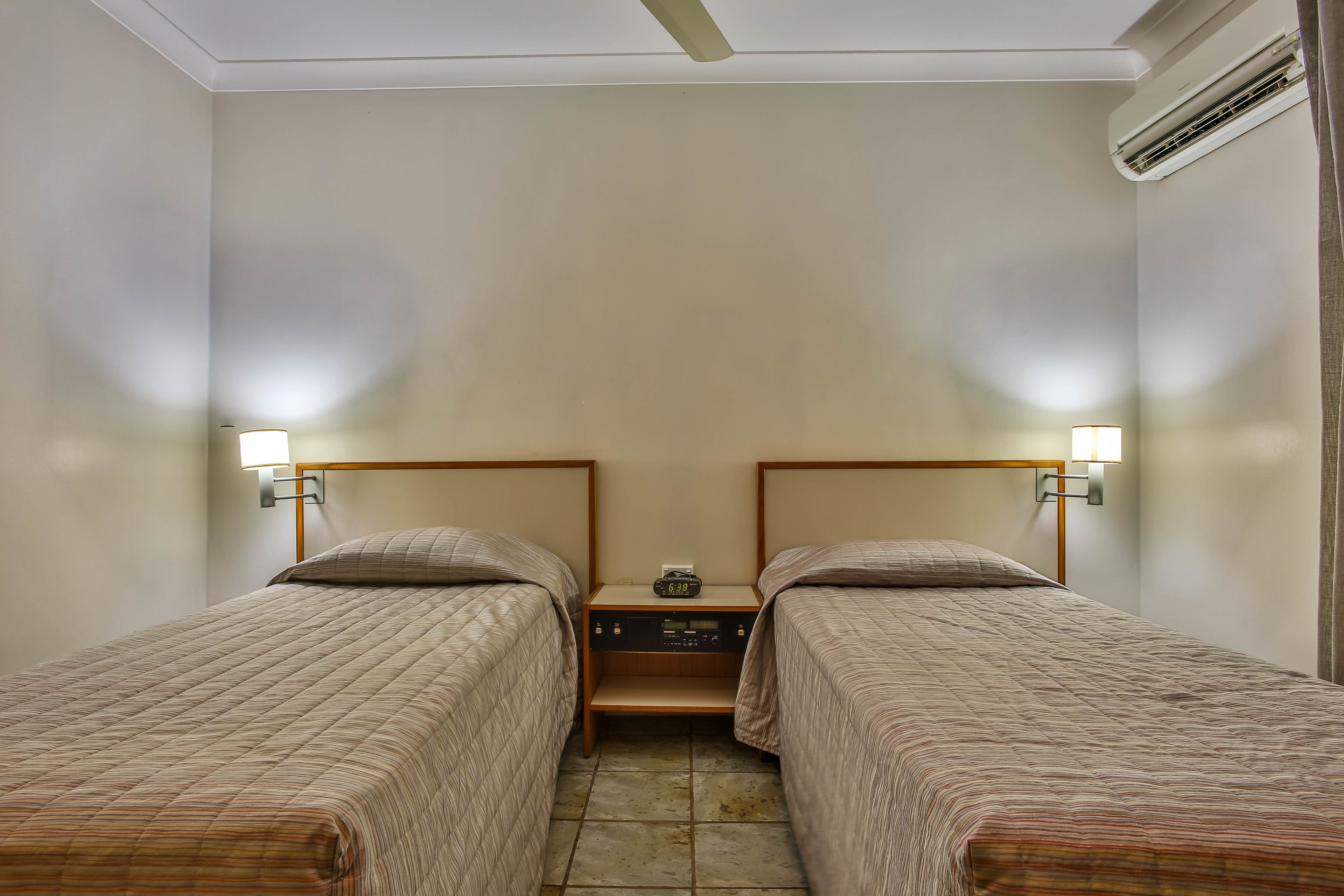A twin room with two single beds, a nightstand with a clock, and a ceiling fan.