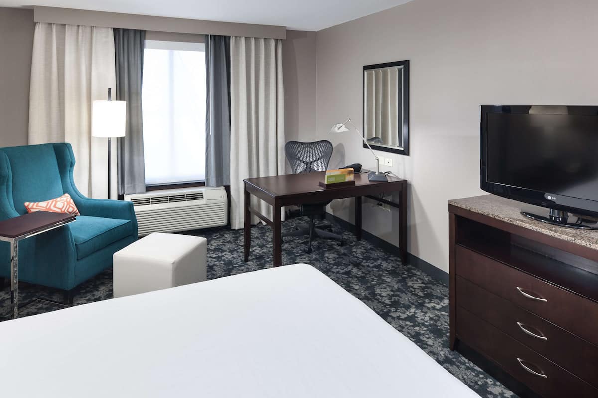 A hotel room with a bed, a desk, a chair, a TV, and a window with curtains.