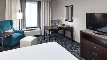 A hotel room with a bed, a desk, a chair, a TV, and a window with curtains.