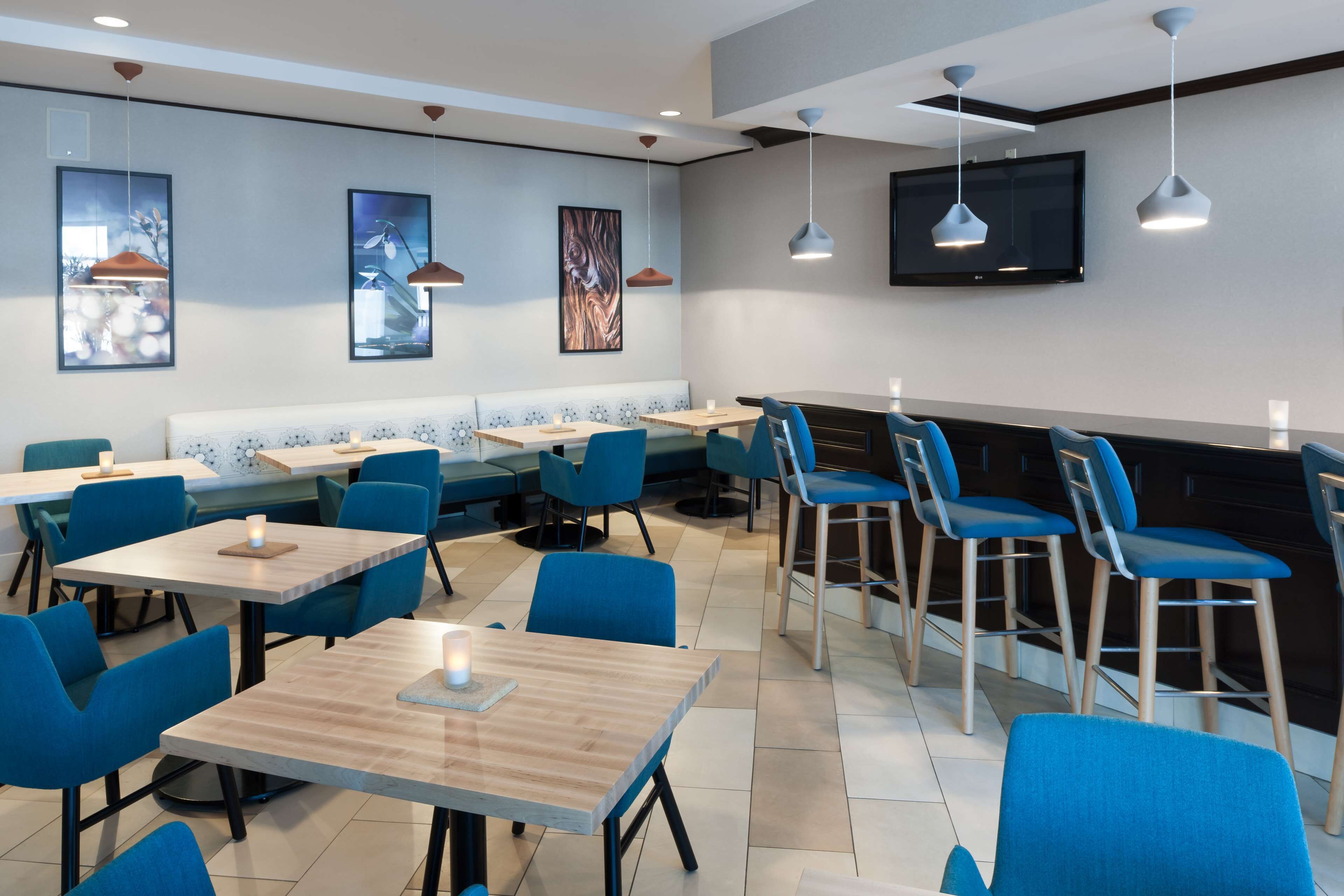 A modern restaurant with blue chairs and wooden tables, a flat-screen TV on the wall, and artwork on the walls.