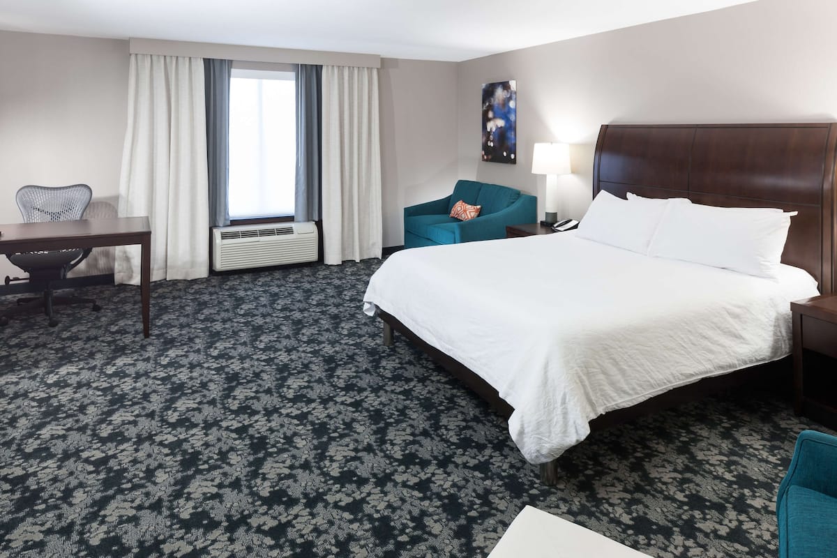 A hotel room with a large bed, a desk, a chair, and a window with curtains.