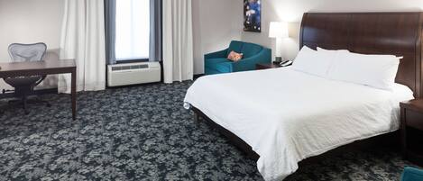 Habitación de hotel con una cama grande, un escritorio, una silla y una ventana con cortinas.